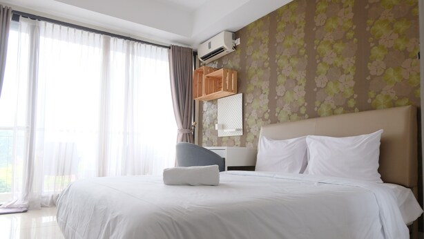 Hotellihuone, jossa on suuri sänky, työpöytä ja tuoli. Huoneessa on ikkuna, jossa on verhot, ilmastointilaite ja kukkakuviotapetti.