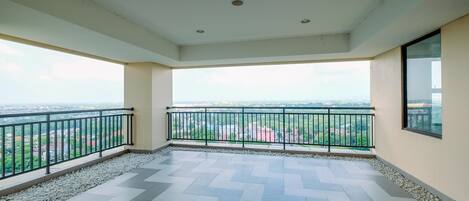 A spacious balcony with a tiled floor and a railing, offering a view of a cityscape.