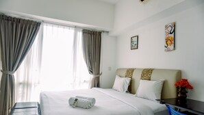 Una habitación de hotel con cama, escritorio, silla y ventana con cortinas.