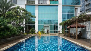 Una piscina interior con suelo de baldosas azules, rodeada de follaje y un edificio moderno con grandes ventanales al fondo.