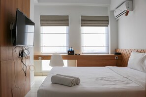 Een hotelkamer met een bed, een bureau, een televisie en een raam met jaloezieën.