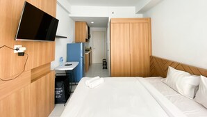 A hotel room with a bed, a desk with a chair, a television mounted on the wall, and a wardrobe.