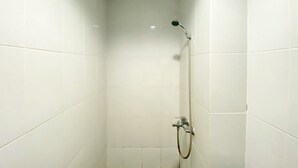A small, white-tiled shower room with a handheld showerhead and a fixed showerhead.