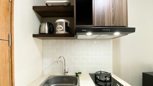 A kitchen with a stainless steel sink, a gas stove, and a coffee maker on a wooden shelf.