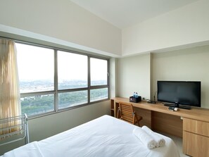 A hotel room with a large window, a bed, a desk with a TV, and a chair.