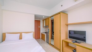 A hotel room with a bed, a TV on a wooden stand, a kitchenette, and a sliding door closet.