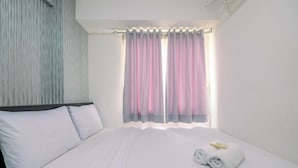 A neatly made bed with white linens, a headboard, and a window with sheer curtains.