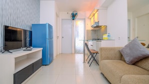 A modern kitchen with a blue refrigerator, a TV on a wooden stand, and a glass dining table with chairs.