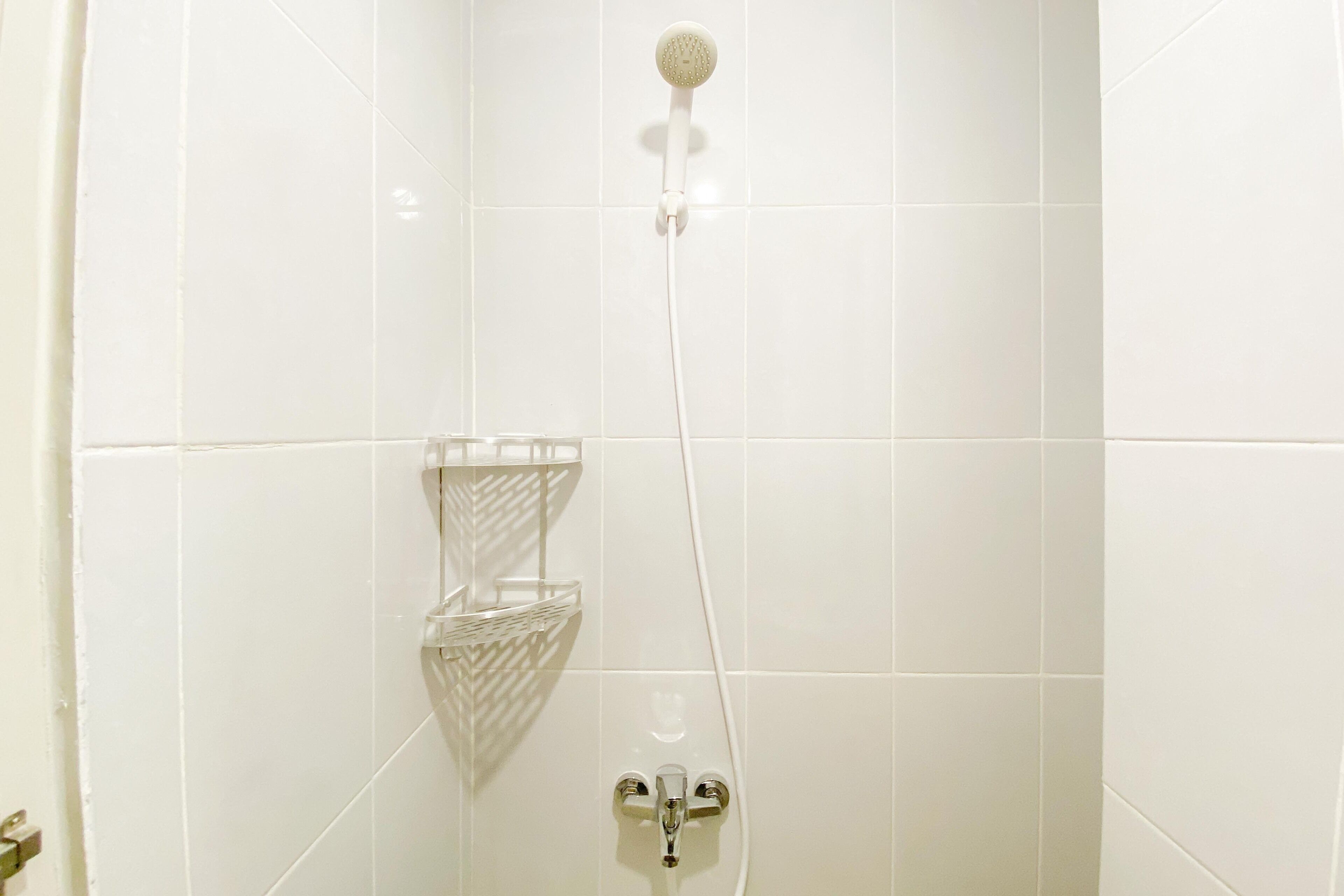 Un baño con paredes de azulejos blancos, un cabezal de ducha, un rociador de mano y un grifo empotrado.