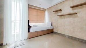 A modern bedroom with a bed, a window with curtains, a wooden nightstand, and built-in shelves. - Cozy Stay Studio Room Apartment At B Residence (Pagedangan)
