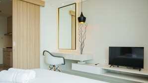 A modern hotel room with a bed, a TV, a mirror, and a wooden door. - Cozy And Homey Studio At Bintaro Embarcadero Apartment (South Tangerang)