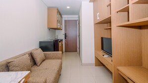 Un espacio habitable compacto con un sofá, un televisor sobre un mueble de madera y una kitchenette con armarios y un refrigerador.