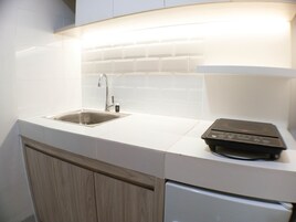 Una cocina con un lavamanos de acero inoxidable, una placa de cocción por inducción negra y muebles de cocina blancos.