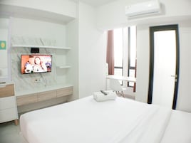 Una habitación de hotel moderna con una televisión de pantalla plana montada en una pared de mármol, una cama con edredón blanco, una mesita de noche con un control remoto y una ventana con cortinas.