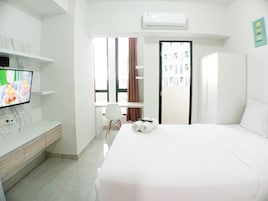 Habitación de hotel con cama, televisor en un mueble bajo, escritorio con silla y ventana con cortinas.