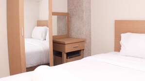 A hotel room with a bed, a wooden nightstand with a mirror, and a small drawer. - Elegant And Strategic Loft Studio Apple 1 Condovilla Apartment (Jakarta)