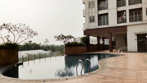 A swimming pool with a curved edge, surrounded by a tiled deck. - Comfort And Warm Studio At Serpong Greenview Apartment (South Tangerang)