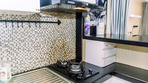 A kitchen with a gas stove, a tiled backsplash, and a black countertop. - Comfort And Warm Studio At Serpong Greenview Apartment (South Tangerang)