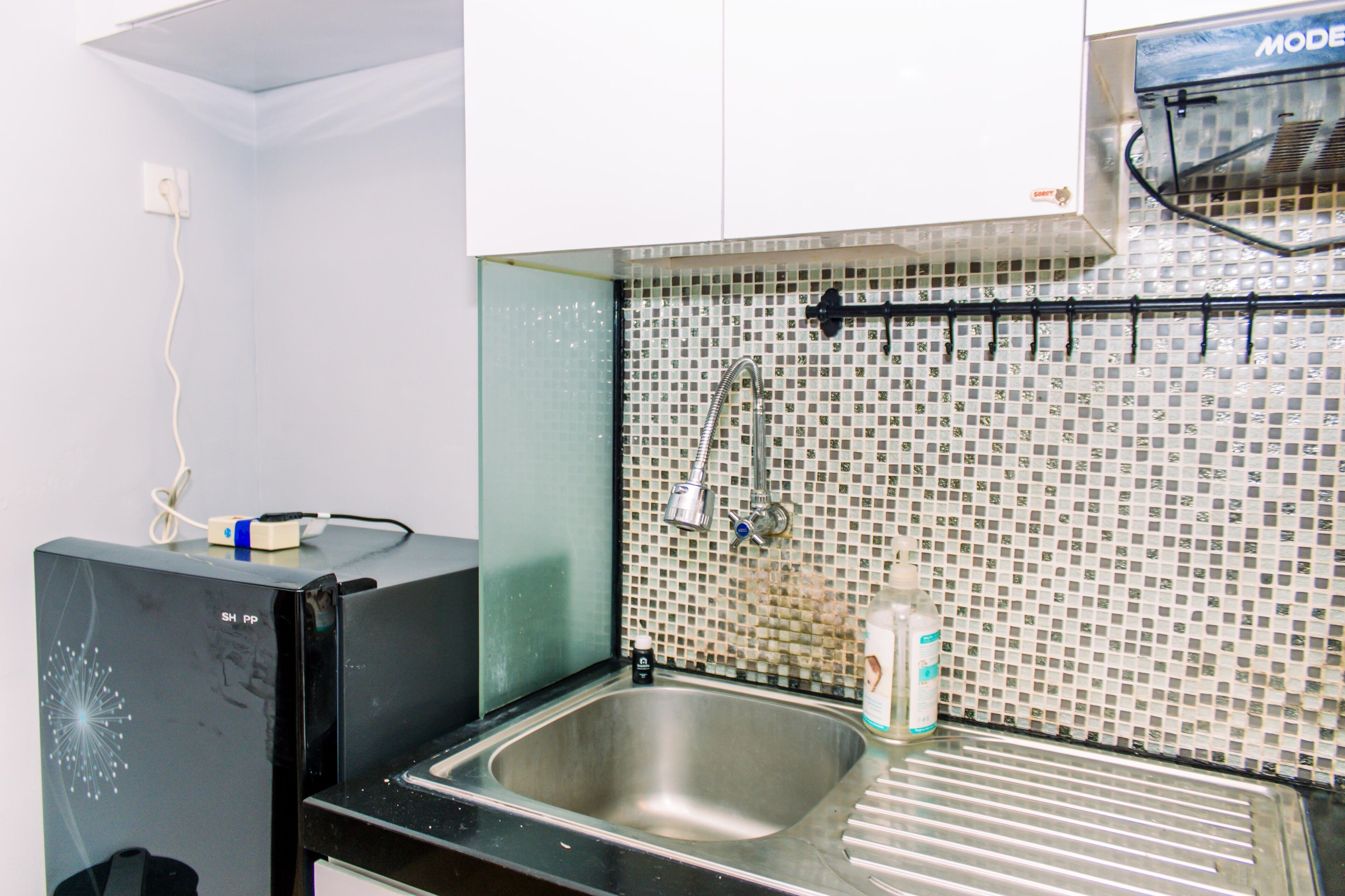 A kitchen with a stainless steel sink, a tiled backsplash, and a black refrigerator.
