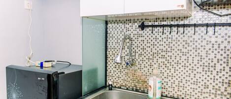 A kitchen with a stainless steel sink, a tiled backsplash, and a black refrigerator.