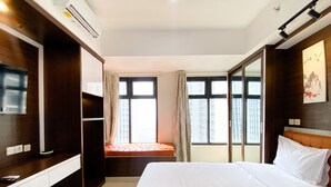 Habitación de hotel con cama, televisión, ventana con cortinas y vistas a edificios.