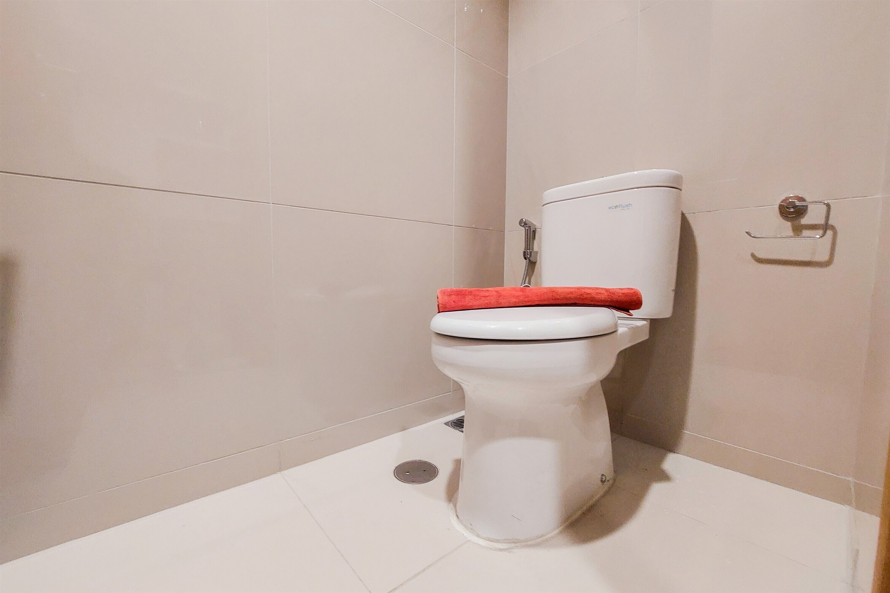 A standard white toilet with a red seat in a bathroom with beige tiles.