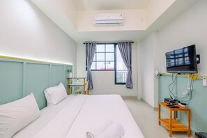 Habitación de hotel con cama, televisor montado en la pared, una mesita con regleta de enchufes y ventana con cortinas.