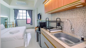 Una habitación de hotel compacta con cama, kitchenette pequeña, lavamanos y televisor.