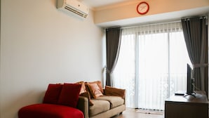 Un soggiorno con divano, una poltrona rossa, televisore e un balcone con tende.