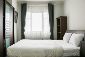 Enjoy a restful stay in this cozy room featuring a comfortable bed, ample wardrobe space, and a window with sheer curtains.