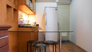 Una cucina compatta con un tavolo in vetro, due sgabelli e un frigorifero bianco.
