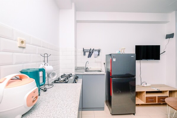 A compact kitchen with white tiled walls, a grey countertop, a black refrigerator, a teal kettle, and a small sink.
