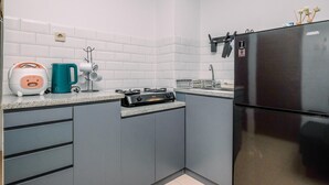 A kitchen with grey cabinets, a black refrigerator, a stove, a kettle, and a coffee maker. - Comfy And Elegant 2Br Tifolia Apartment Pulomas Rawamangun (Jakarta)