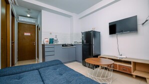A compact living space with a kitchenette, a sofa, a small round table, and a TV mounted on the wall. - Comfy And Elegant 2Br Tifolia Apartment Pulomas Rawamangun (Jakarta)