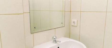 Ein Badezimmer mit einem weißen Waschbecken, einem Spiegel und einem Lichtschalter an der Wand.