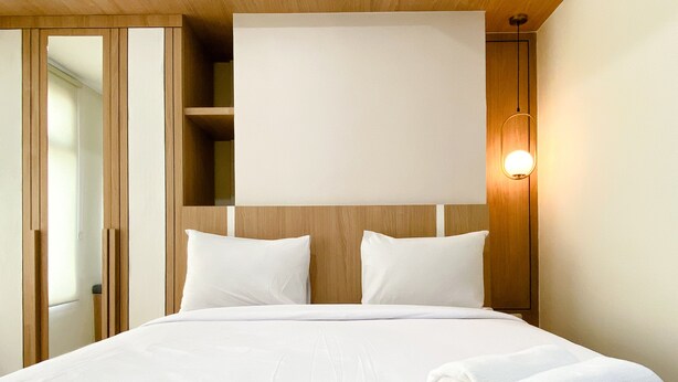 Habitación de hotel con una cama grande, dos almohadas, cabecera de madera y una lámpara de pared.