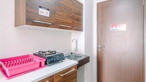 A kitchen with wooden cabinets, a sink, a countertop with a kettle, and a pink dish rack. - Cozy And Modern Look Studio Transpark Juanda Bekasi Timur Apartment (Bekasi)