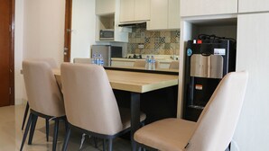 A modern kitchen with a dining area, featuring a refrigerator, microwave, and tiled backsplash. - Scenic And Homey 2Br Signature Park Grande Apartment (Jakarta)