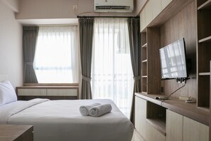 A hotel room with a bed, a TV mounted on the wall, and a window with curtains. - Elegant And Nice Studio Room At Citra Living Apartment (Jakarta)