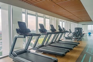 Ett gym med löpband, träningsutrustning och stora fönster med utsikt över staden.