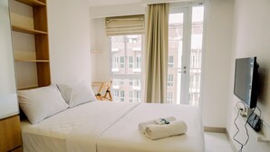 Habitación de hotel con cama, televisor, ventana con cortinas y vistas a edificios.