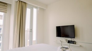 Habitación de hotel con cama, televisor montado en la pared y ventana con cortinas.
