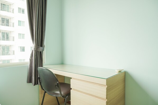 A small, modern office space with a glass desk, a single chair, and a window with curtains. - Comfortable And High Floor 2Br Apartment At Thamrin Residence (Jakarta)