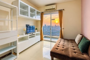 A modern living room with a sofa, TV, and a balcony with a city view. - Comfortable And High Floor 2Br Apartment At Thamrin Residence (Jakarta)