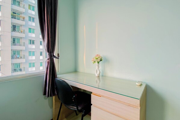 A room with a glass desk, a black chair, a vase with flowers, and a view of a building with balconies. - Comfortable And High Floor 2Br Apartment At Thamrin Residence (Jakarta)