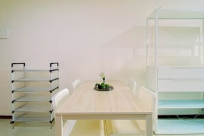 A room with a wooden table, white chairs, a white shelving unit, and a metal ladder.