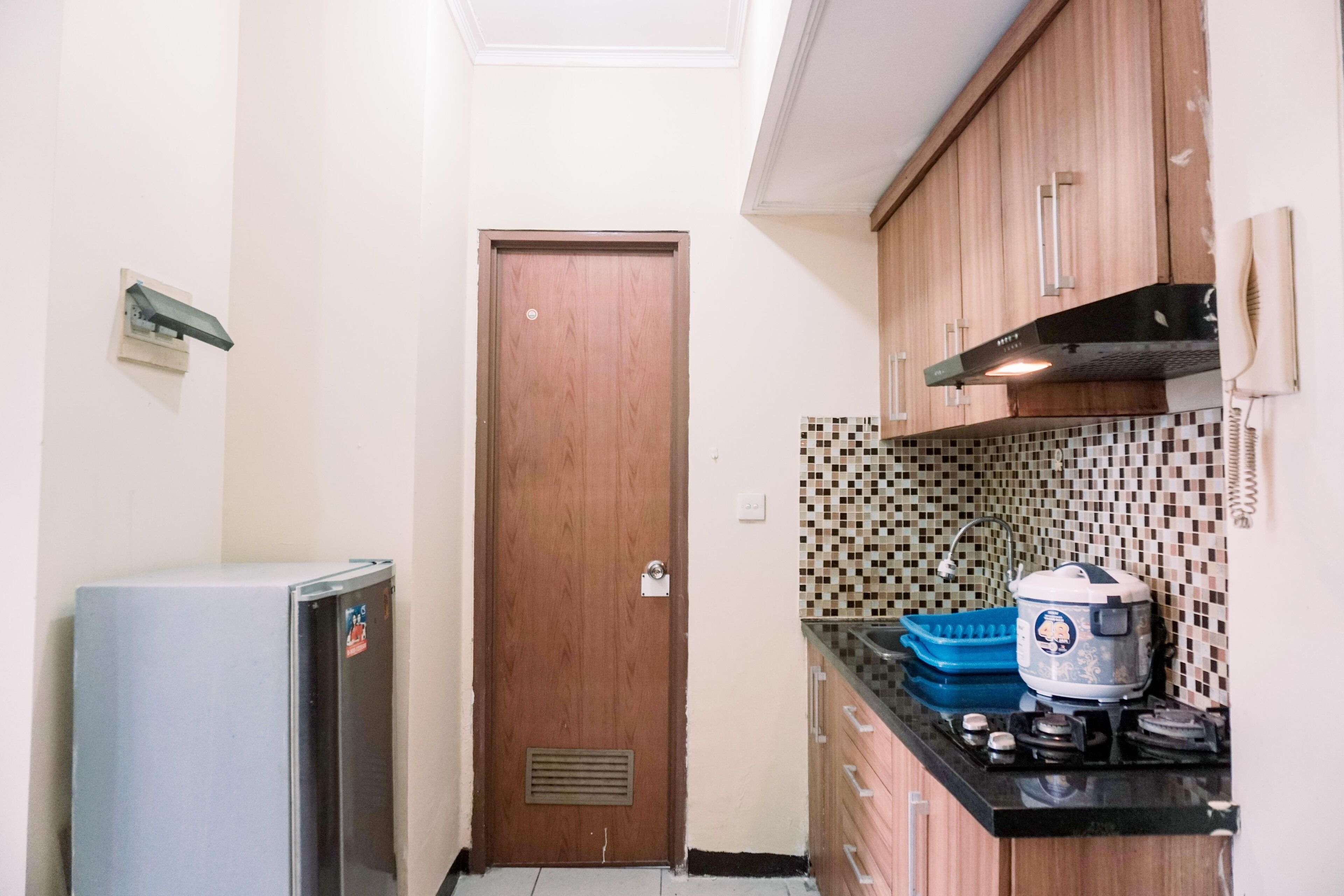 A compact kitchen with wooden cabinets, a tiled backsplash, a built-in stove, and a refrigerator.
