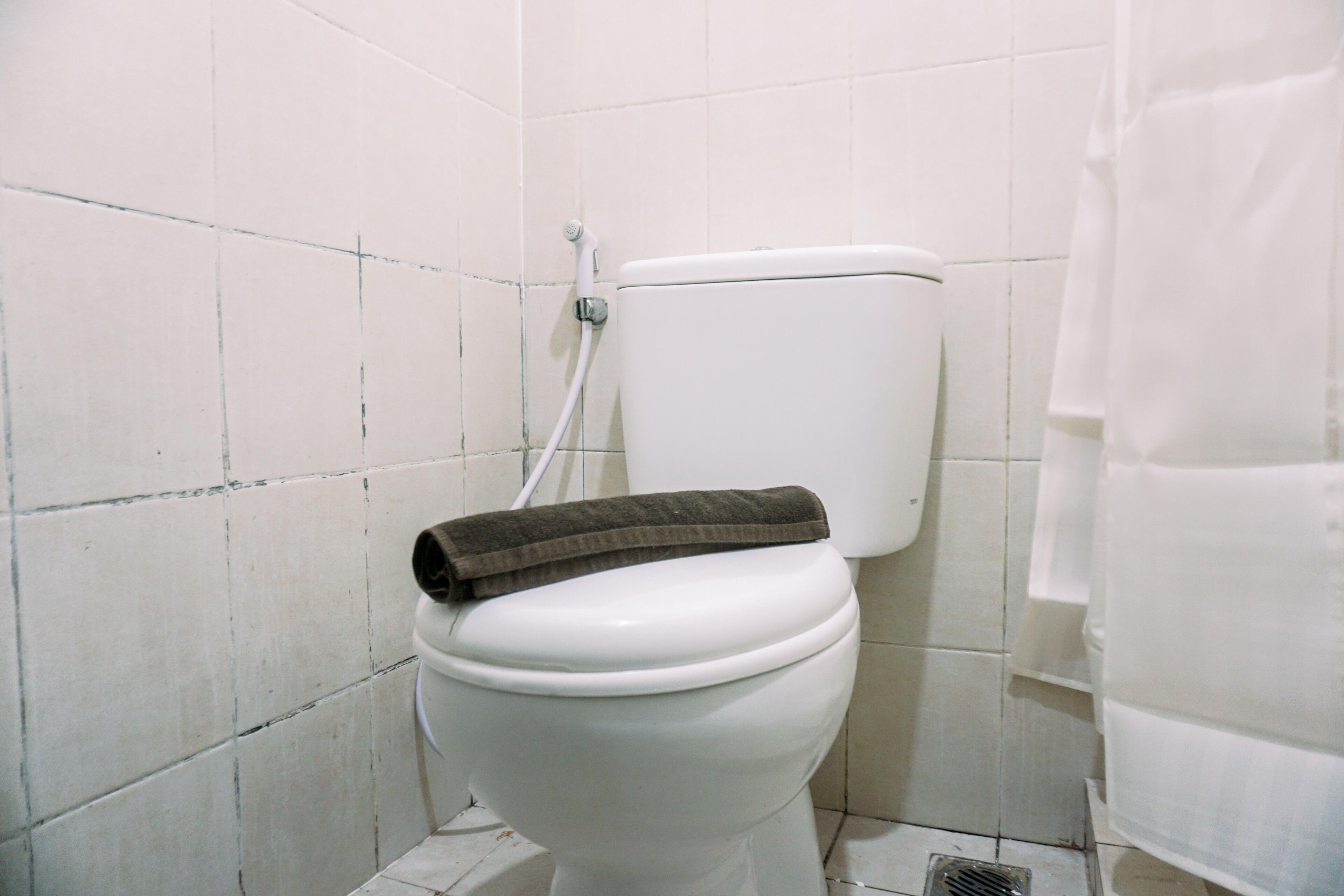 A white toilet with a towel on top, a shower curtain, and tiled walls.
