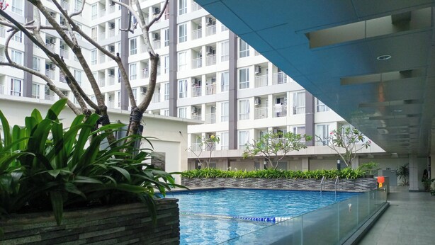 An indoor swimming pool with a stone wall and plants, surrounded by a modern building with balconies. - Cozy Designed Studio At Taman Melati Sinduadi Apartment (Pogung Lor)