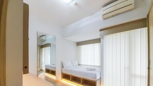 A modern hotel room with a bed, bedside tables, a mirror, and a window with blinds. - Cozy Designed Studio At Taman Melati Sinduadi Apartment (Pogung Lor)